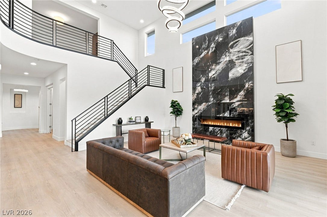 An inviting open-concept living area features soaring ceilings and an elegant marble fireplace, complemented by light wood flooring.