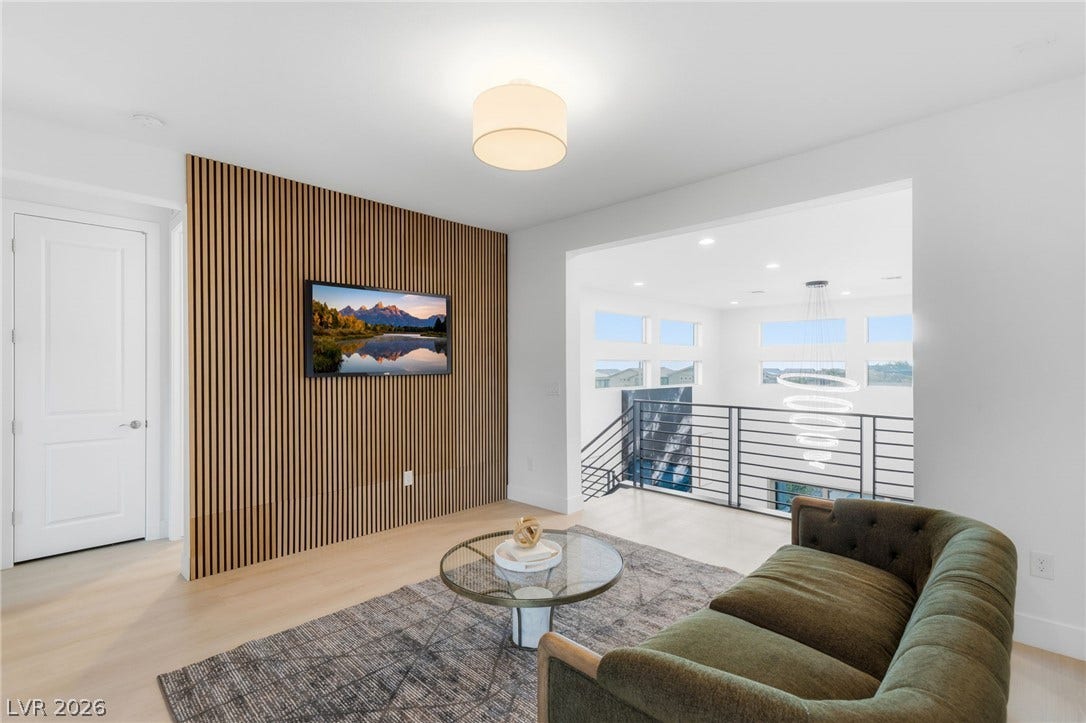 Modern interior living space featuring light wood flooring, a textured accent wall, and a view of an upper-level loft.