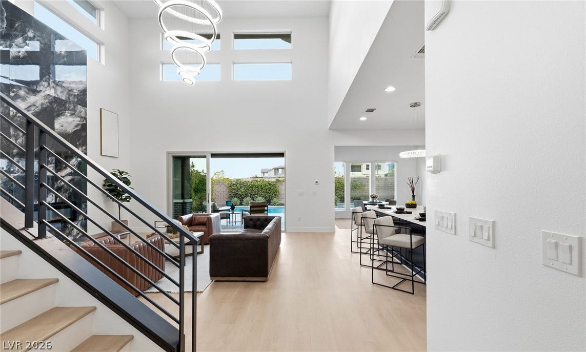 A grand, open-concept living space with soaring ceilings and light wood floors seamlessly connects to an outdoor oasis.