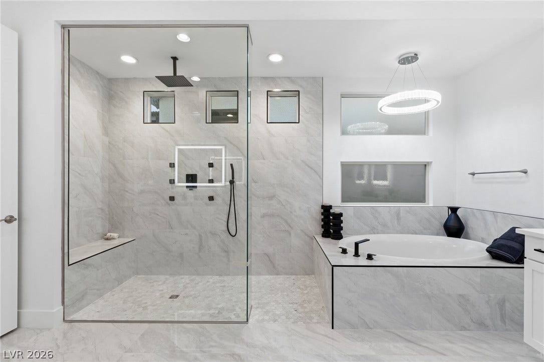 Luxurious bathing experience in this primary bath, featuring an oval soaking tub and a spacious glass-enclosed shower.