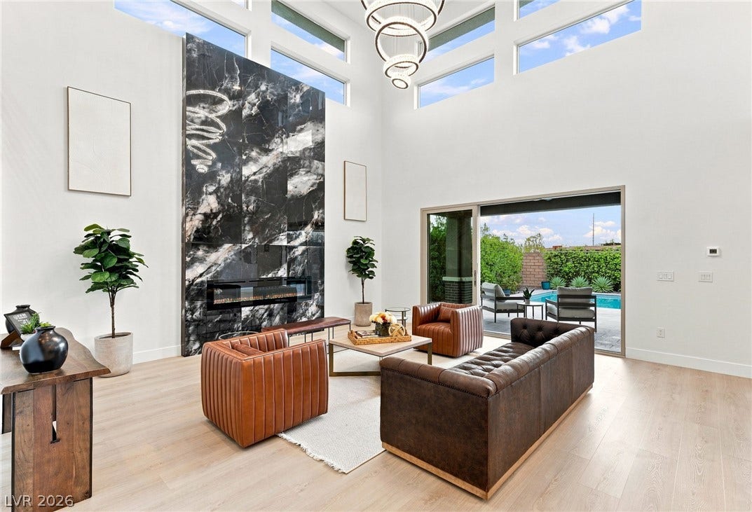 A grand living space with towering ceilings and a striking black marble fireplace, opening to a private pool oasis.