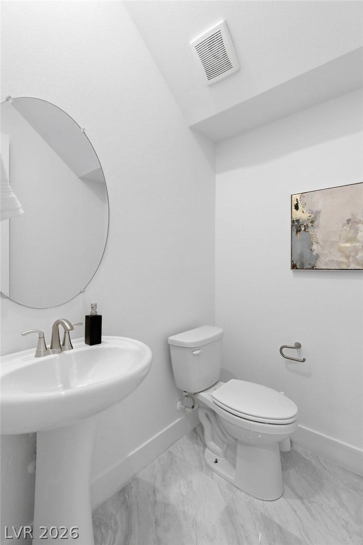 A well-lit powder room showcases a pedestal sink, toilet, and reflective round mirror.