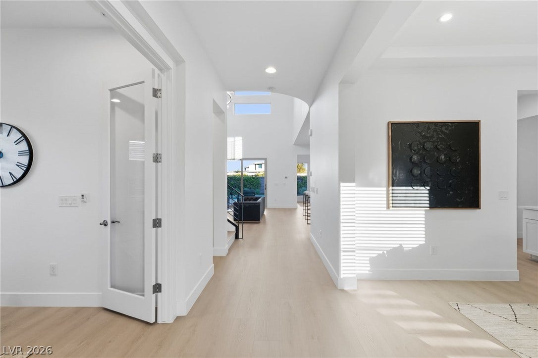 A luminous hallway with soaring ceilings extends towards an inviting living space, framed by clear sightlines and modern design.