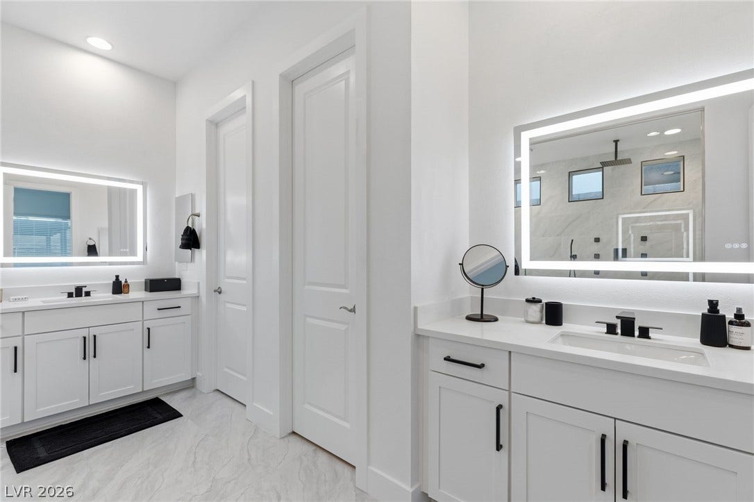 Dual vanities with illuminated mirrors flank a sleek shower, offering a pristine and well-appointed bathing space.