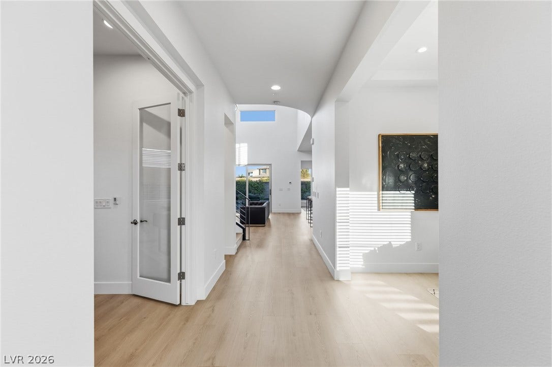 A luminous hallway with rich wood flooring leads to an open-concept living area with abundant natural light.