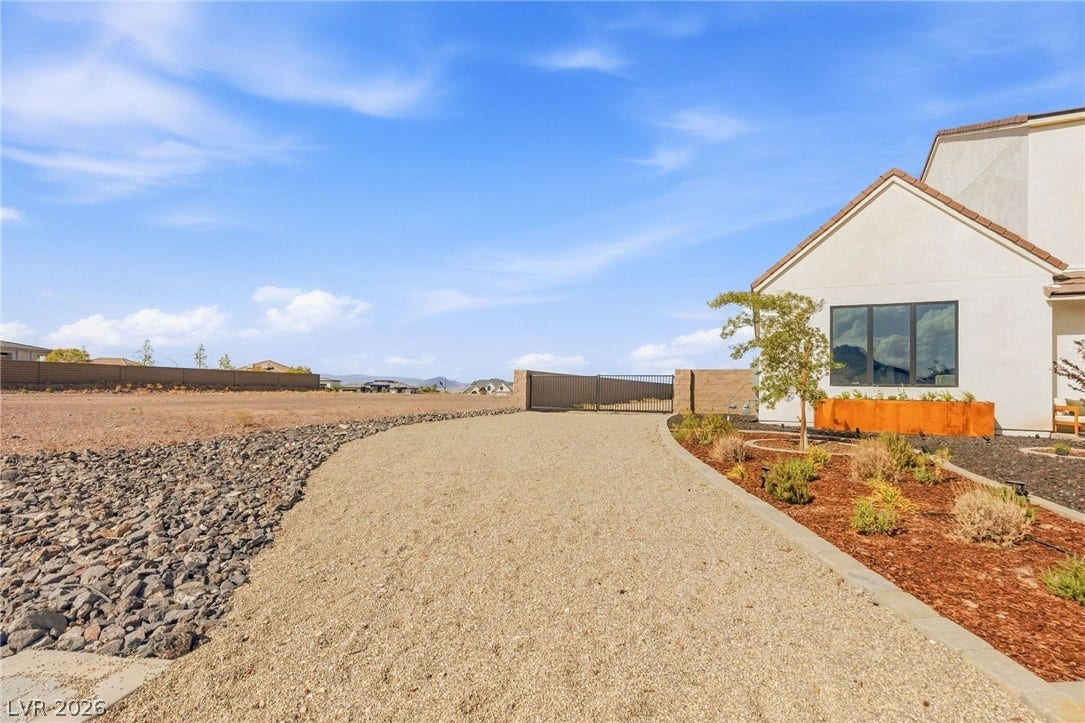 324 Wanda Road, Henderson, NV 89002 A gravel driveway winds past landscaped beds toward a gated entrance under wide skies.