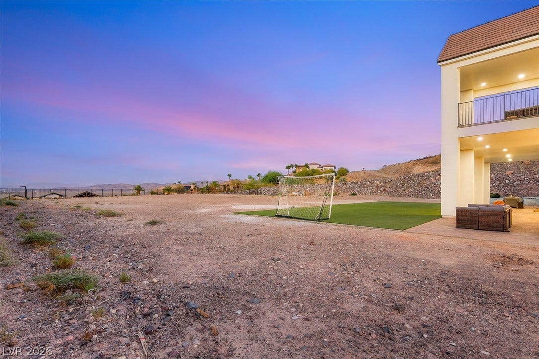 324 Wanda Road, Henderson, NV 89002 A spacious desert lot borders the multi-level home under a vibrant sunset sky.