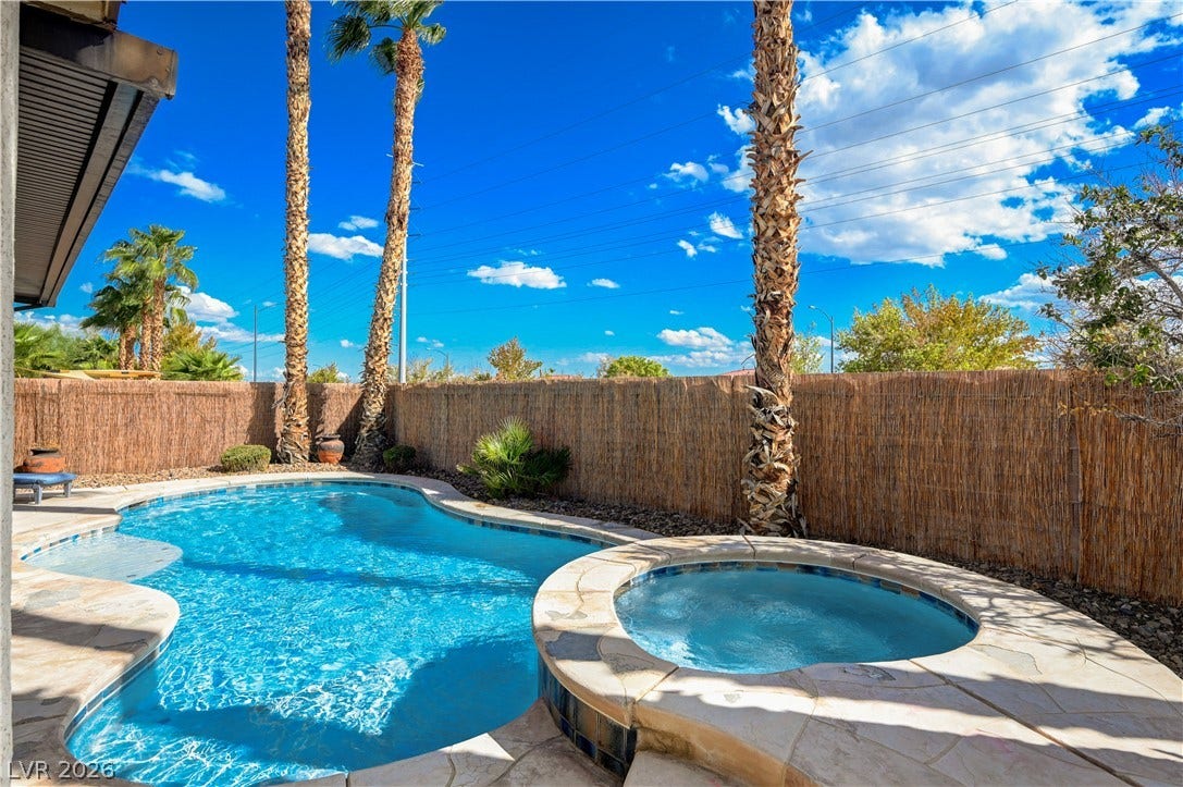 An inviting backyard oasis features a shimmering pool and elevated spa framed by towering palm trees.
