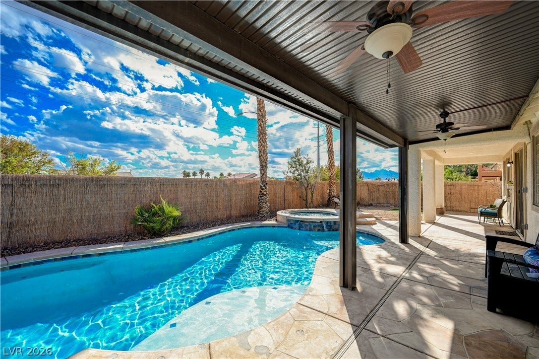 An inviting backyard oasis features a shimmering swimming pool alongside a covered stone patio.