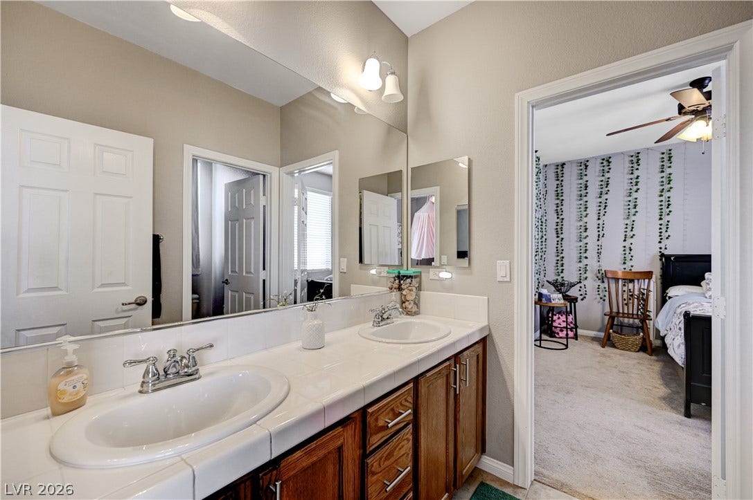 A spacious double vanity features classic wood cabinetry and pristine white tiled countertops.