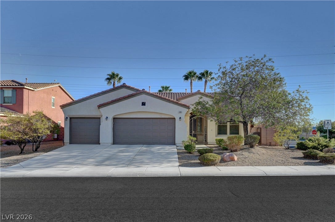 A spacious driveway leads to three garage bays alongside low-maintenance desert landscaping under blue skies.
