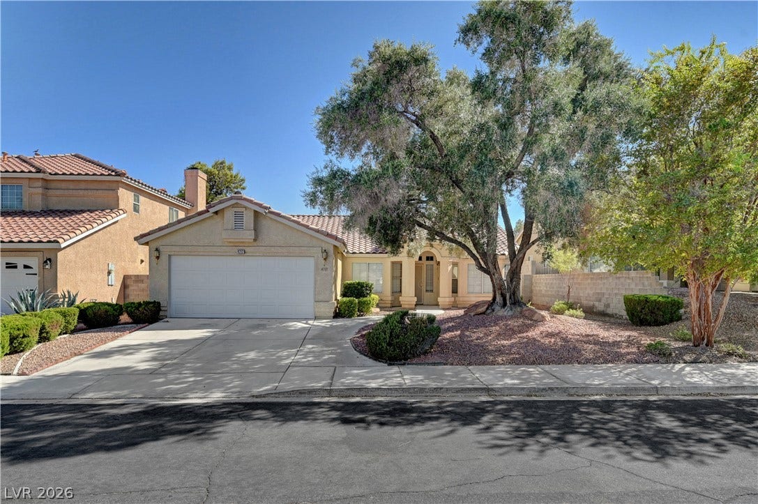 Mature trees shade the front yard of this stucco residence featuring a tile roof.