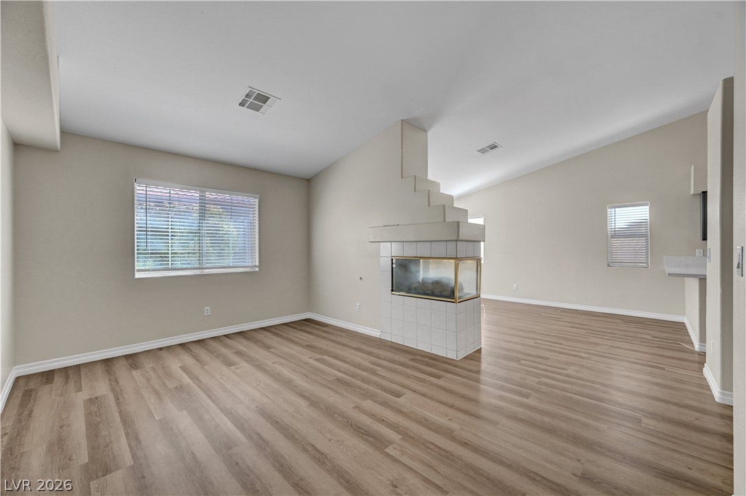 Vaulted ceilings and a three-sided fireplace highlight this open living area with wood-style flooring.