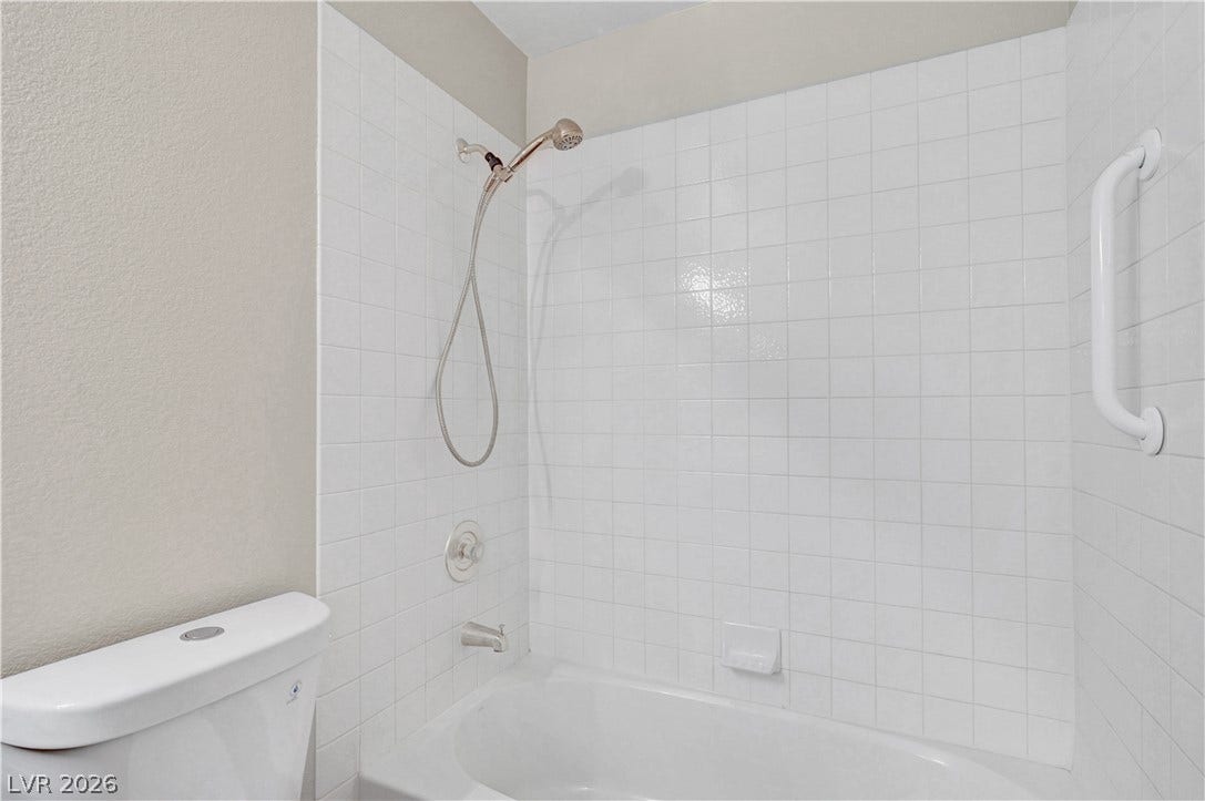 Crisp tiled walls enclose a classic tub and shower combination with an integrated safety grab bar.