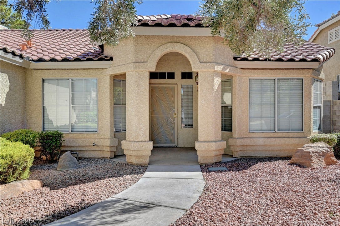 An arched covered entryway welcomes guests along a concrete pathway leading to the front door.