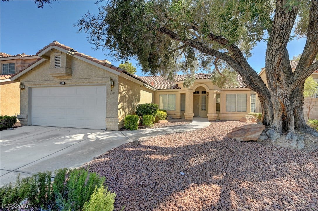 A classic stucco exterior features a tile roof and a mature front yard tree.