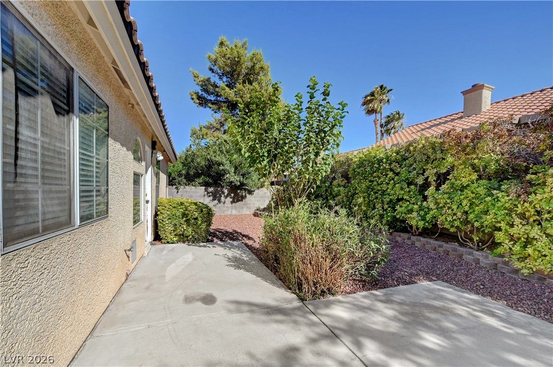 Mature landscaping surrounds a concrete patio area alongside the stucco exterior.