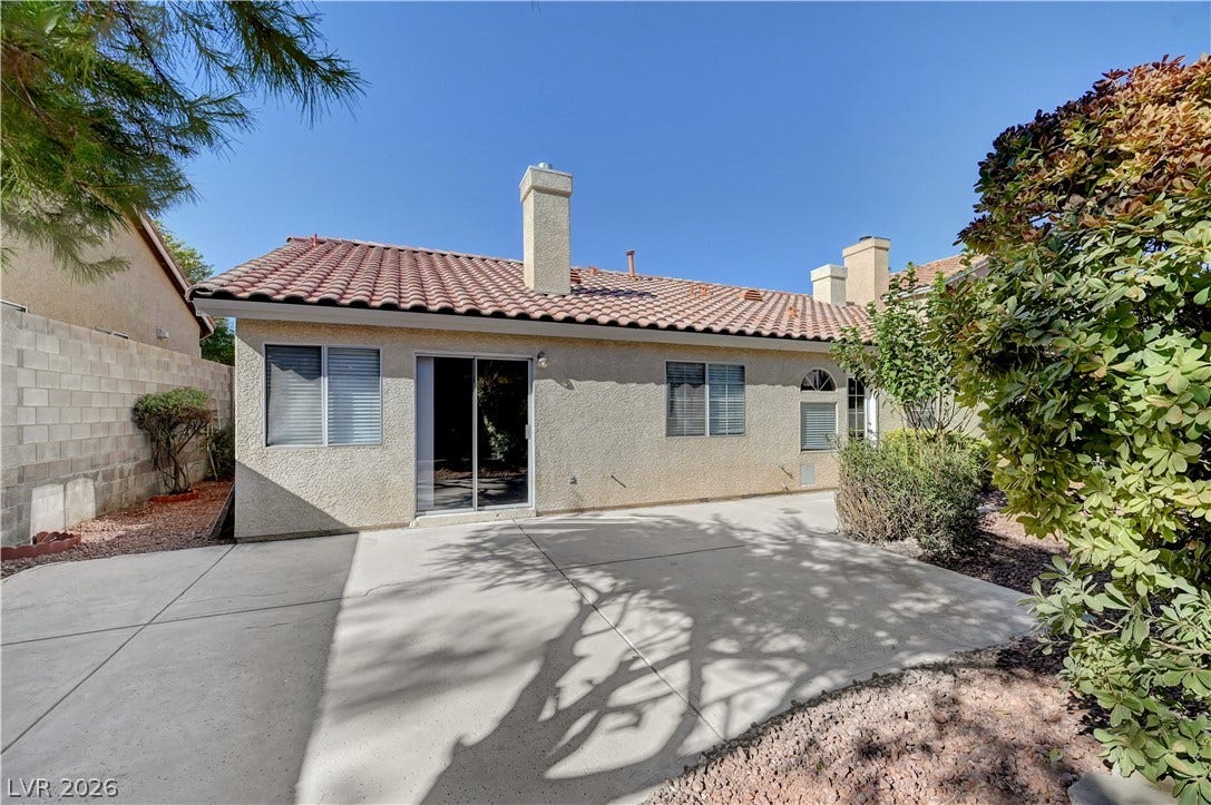 A spacious concrete patio stretches behind this stucco home topped with Spanish tile roofing.