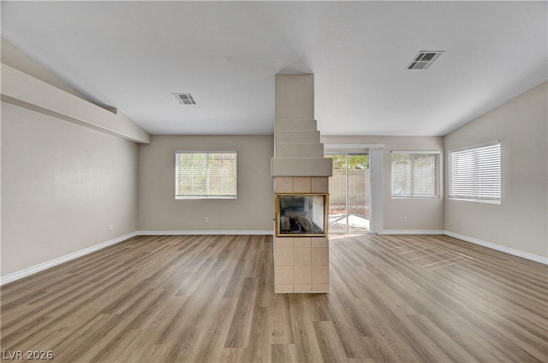 An open living space highlights wood-style flooring and a central three-sided fireplace.