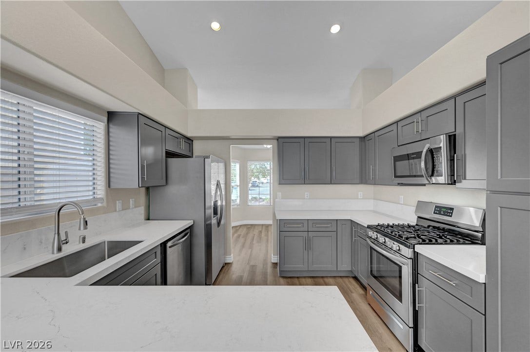 Gleaming stone countertops and modern cabinetry frame this open kitchen with high ceilings.