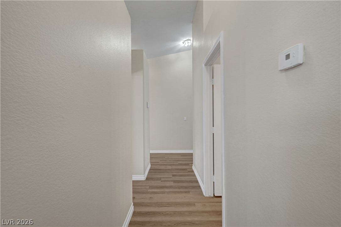 A long hallway connects rooms with crisp baseboards and durable plank flooring.