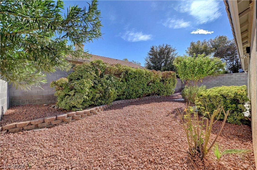 A low-maintenance gravel yard features structured retaining walls and established privacy hedges under open skies.