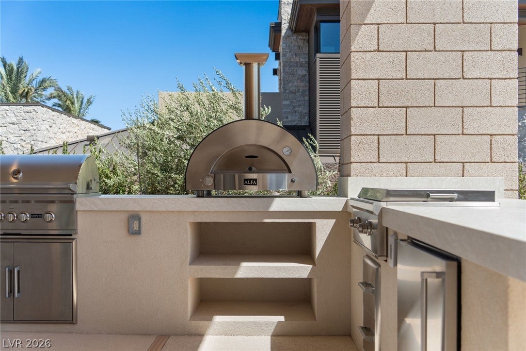 37 Reflection Shores Lane, Henderson, NV 89011 An outdoor kitchen features premium built-in appliances alongside stone masonry accents under clear desert skies.