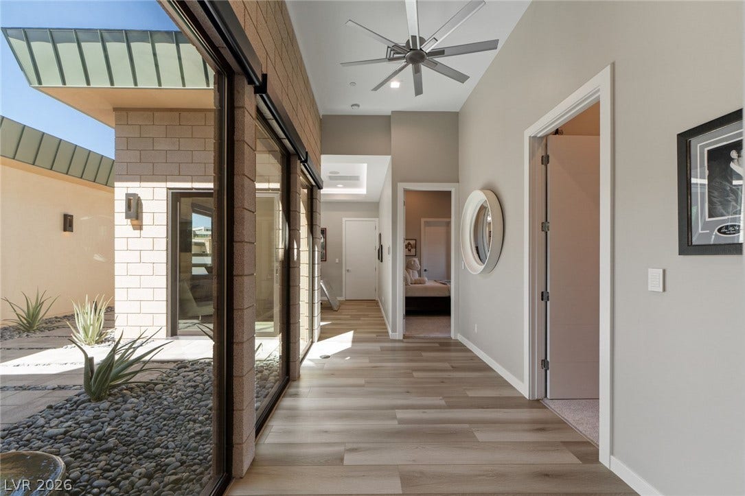 37 Reflection Shores Lane, Henderson, NV 89011 Gleaming wood floors line a sunlit hallway overlooking a modern gravel courtyard.