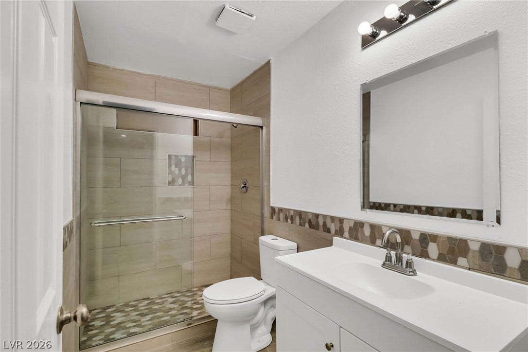 A contemporary vanity with stone counters complements the beautifully tiled walk-in shower.