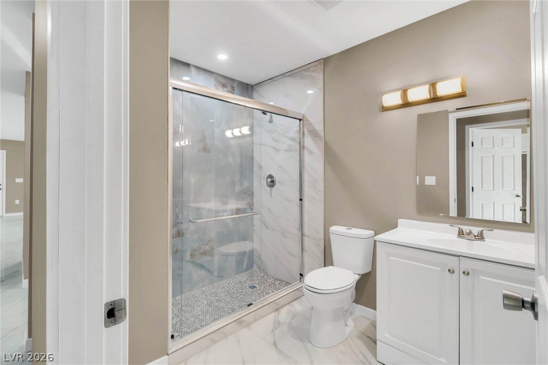 Gleaming stone tile flooring and a glass-enclosed shower elevate this updated bathroom.
