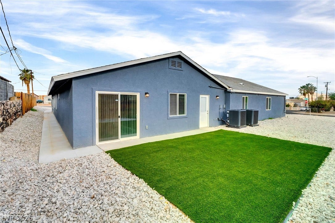 Clean gravel landscaping surrounds a modern synthetic lawn outside this single-story stucco residence.