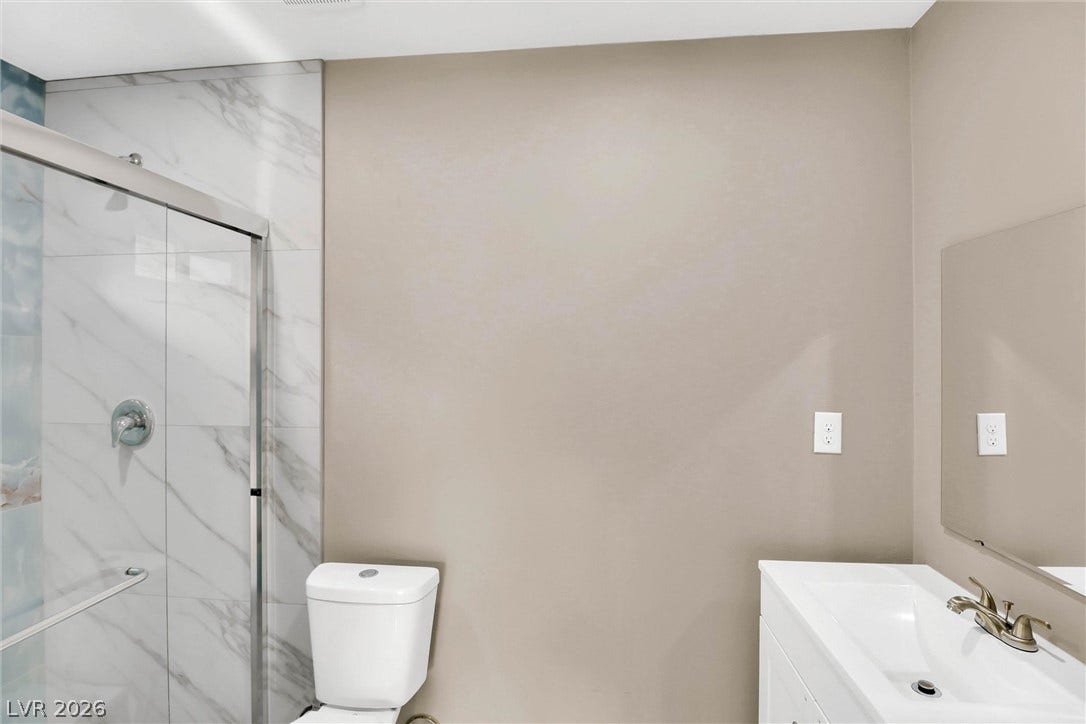 A glass-enclosed walk-in shower with marble-look tile walls anchors this modern bathroom.