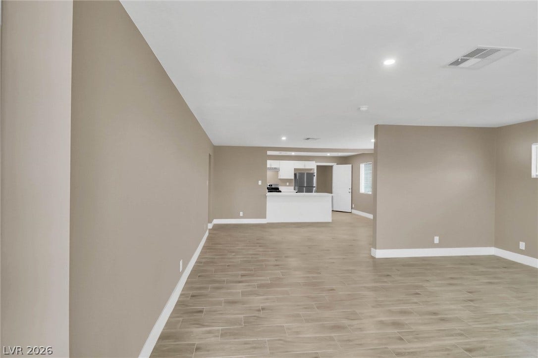 An open layout connects the spacious living area to the kitchen, highlighting plank-style flooring.