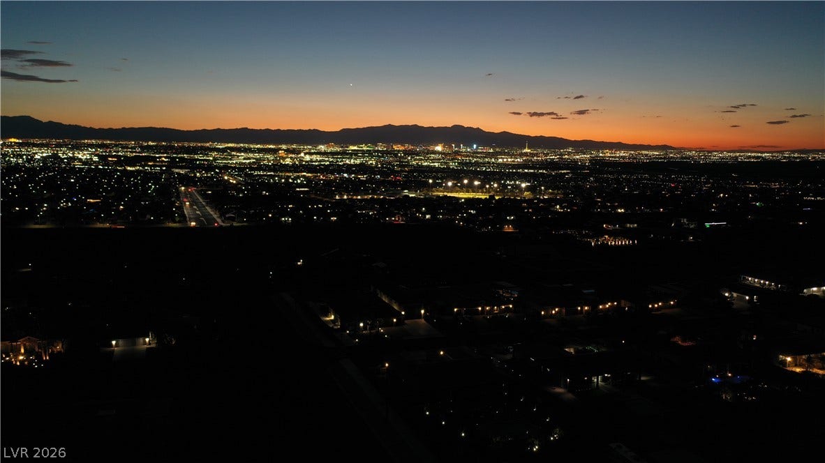 1111 E Warm Springs Road, Henderson, NV 89015 Glittering city lights stretch toward mountain silhouettes under a vibrant twilight sky.