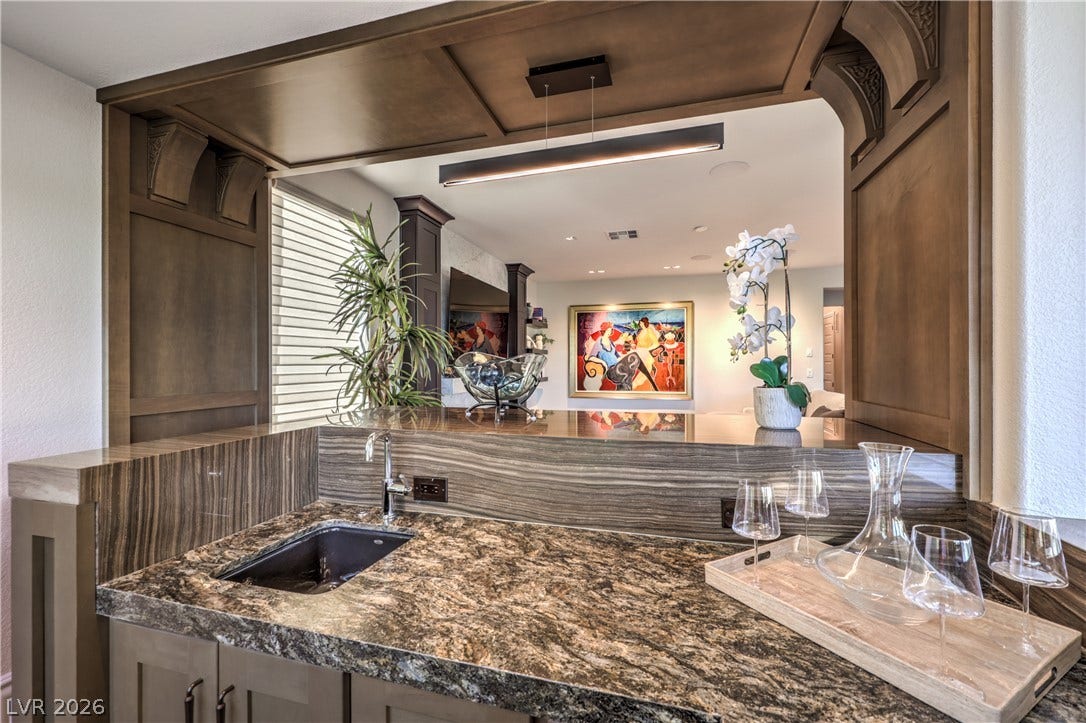 Gorgeous wet bar featuring a beverage refrigerator, sink, custom woodwork, stunning quartzite surfaces and exceptional golf course views.