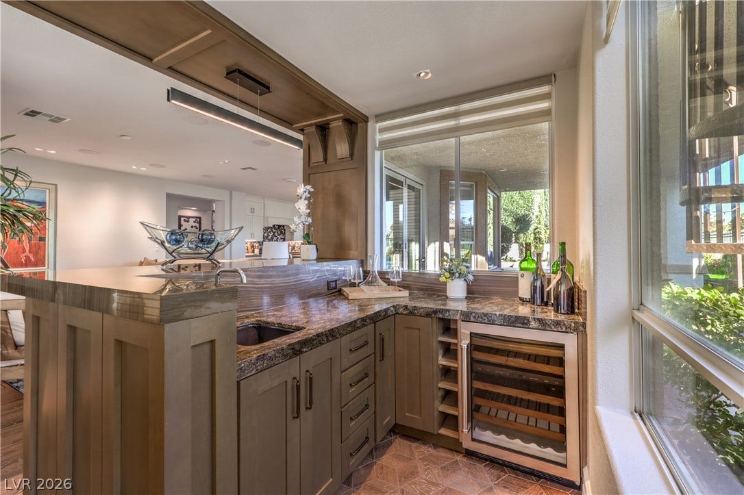 Gorgeous wet bar featuring a beverage refrigerator, sink, custom woodwork, stunning quartzite surfaces and exceptional golf course views.