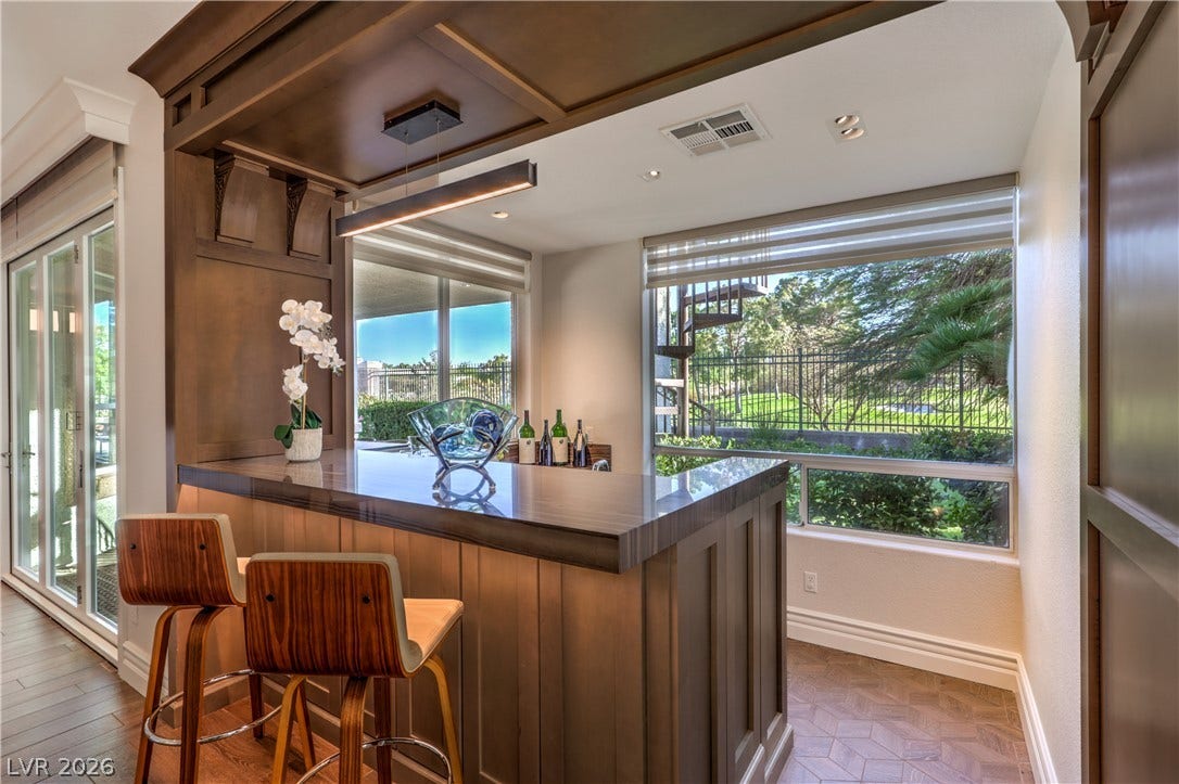 Gorgeous wet bar featuring a beverage refrigerator, sink, custom woodwork, stunning quartzite surfaces and exceptional golf course views.