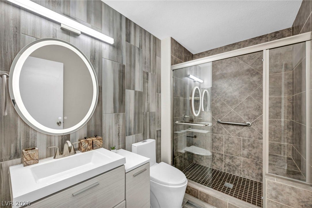 A contemporary bathroom showcases textured wall tiling and a glass-enclosed walk-in shower.