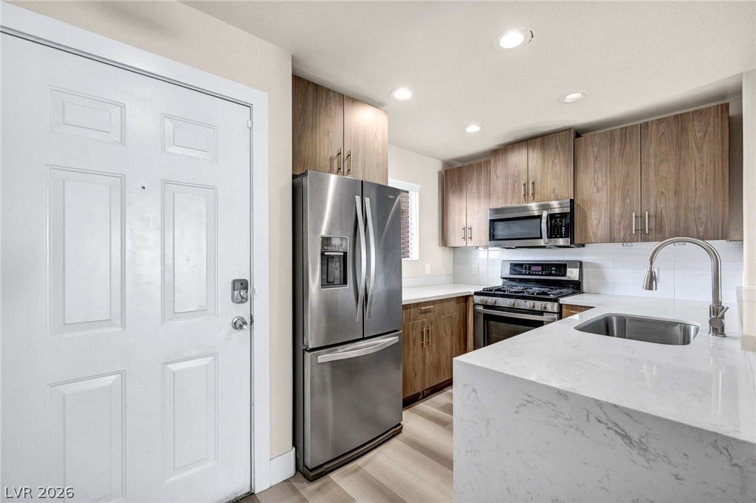 A modern culinary space features warm wood cabinetry, waterfall countertops, and integrated stainless steel appliances.