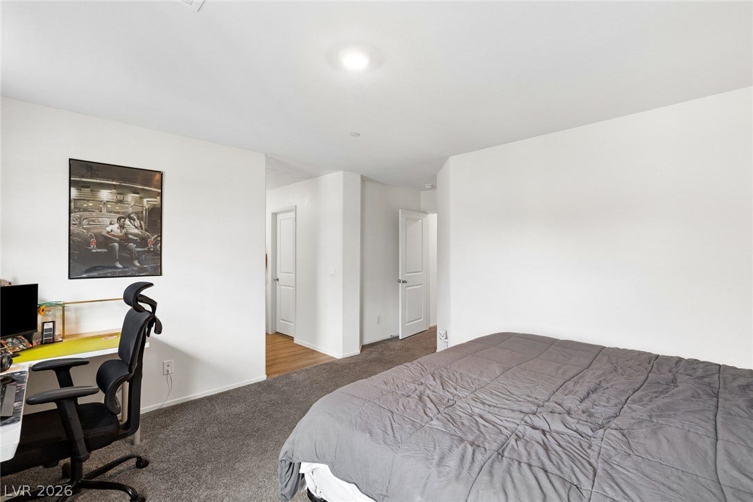 7910 Aurora Sky Street, North Las Vegas, NV 89084 Plush carpeting anchors this quiet bedroom space featuring a doorway to an adjacent hall.