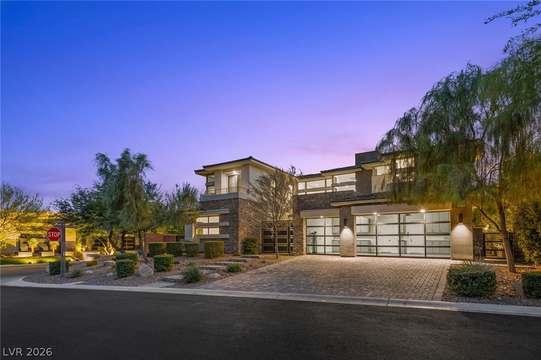11453 Rhodolite Court, Las Vegas, NV 89135 Dramatic modern elevation showcases stone accents and striking glass-paneled garage doors at twilight.