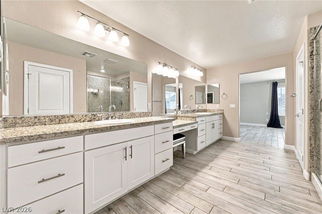 4216 Campriani Avenue, North Las Vegas, NV 89084 Double vanities with stone countertops stand on plank tile flooring inside this bathroom.