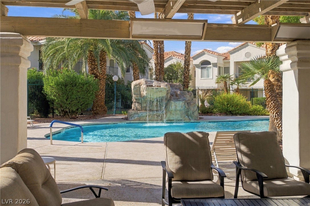 Shaded patio space overlooks a sparkling community pool featuring a rock waterfall and palm trees.
