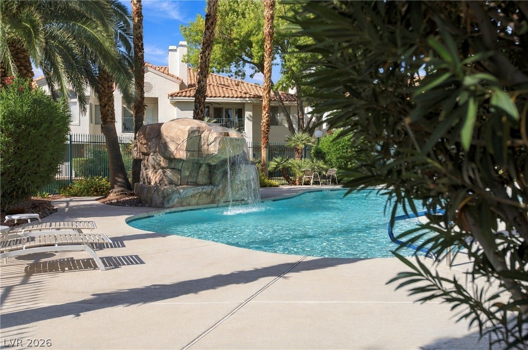 A resort-style swimming pool features a cascading rock waterfall and a spacious concrete sun deck.