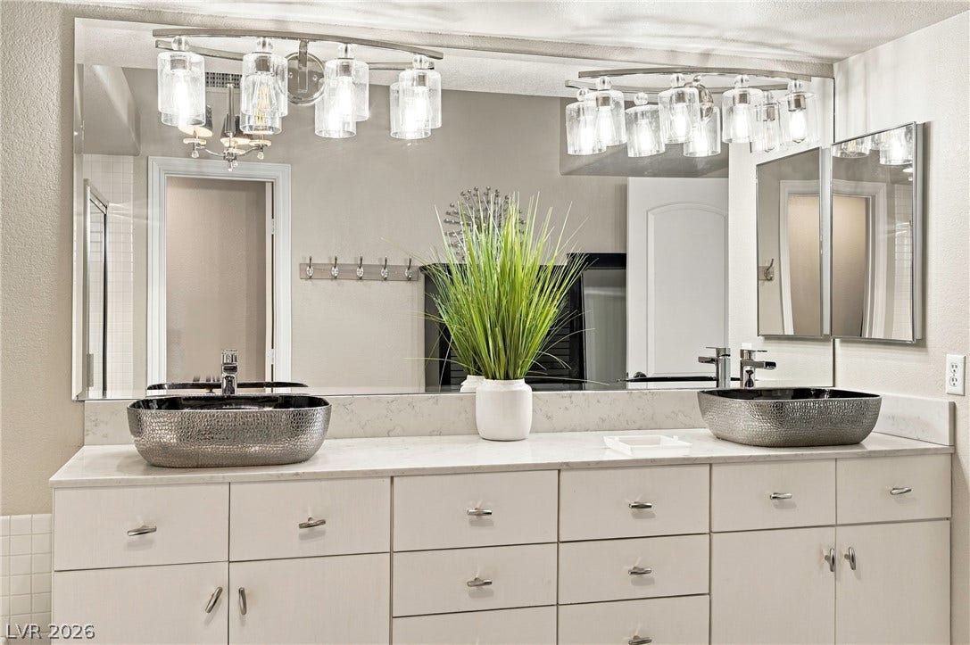 Dual vessel sinks rest on a spacious vanity topped with elegant stone counters.