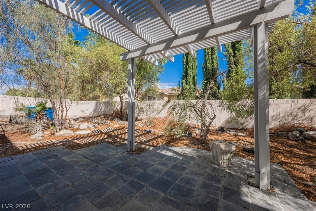 1608 Saddle Rock Circle, Las Vegas, NV 89117 Stone patio tiles lie beneath a structured white pergola overlooking the fenced backyard.