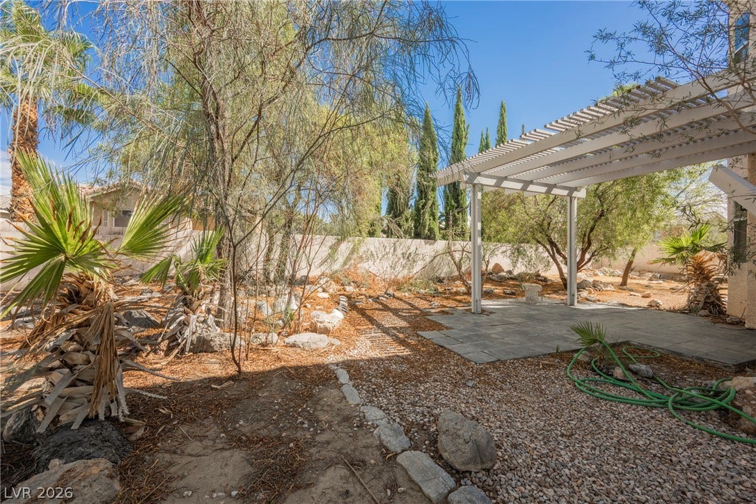 1608 Saddle Rock Circle, Las Vegas, NV 89117 Mature trees frame a paved patio area underneath a white pergola structure.