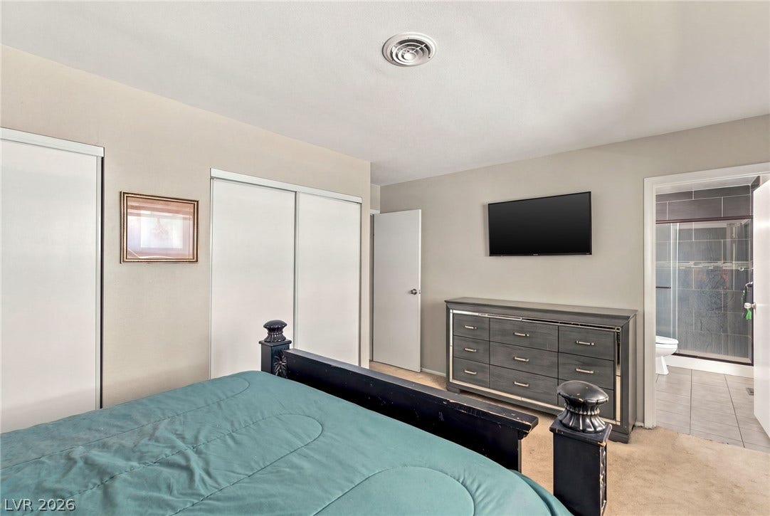 Plush carpeting anchors this spacious bedroom featuring an attached private bathroom with tile floors.