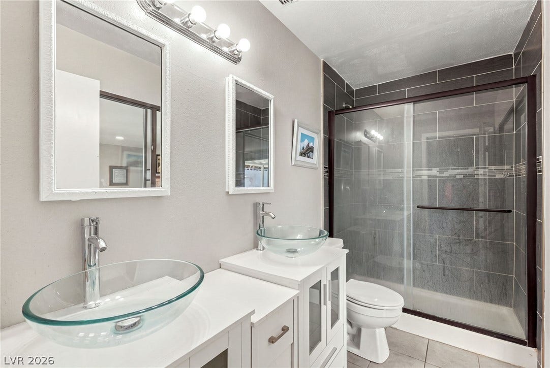 Double vessel sinks stand out alongside a modern glass-enclosed shower with custom tilework.
