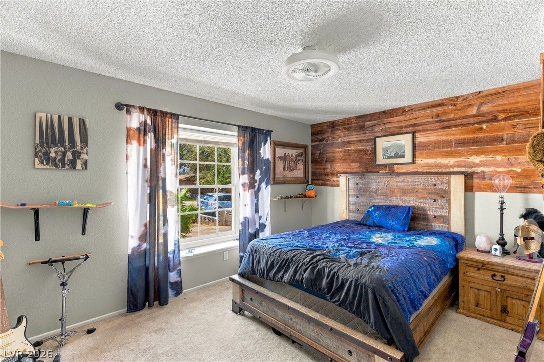 Natural light fills this bedroom featuring a rustic wood accent wall and plush carpeting.